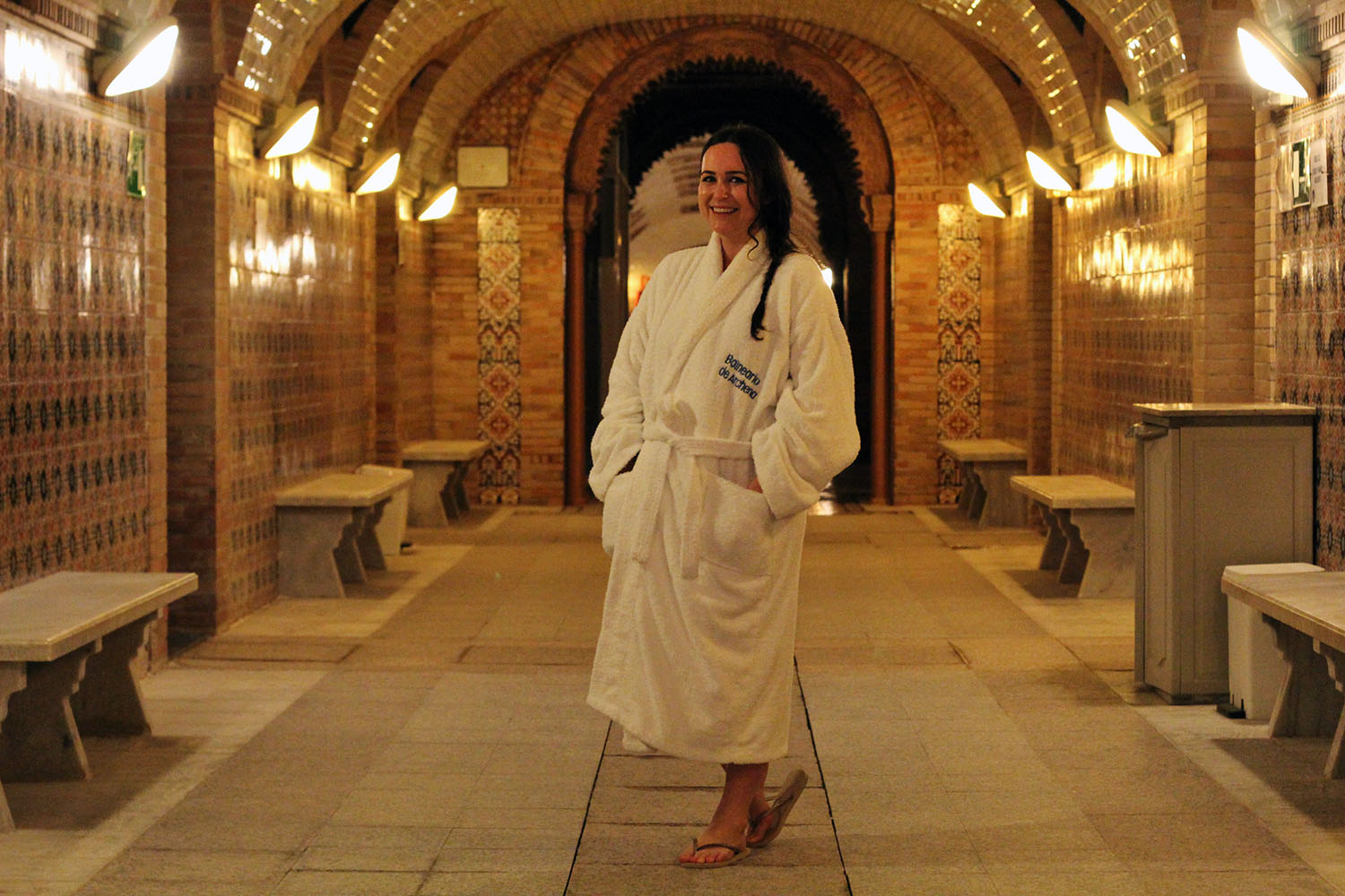 woman in spa robe stands in the underground arched hallway of the spa