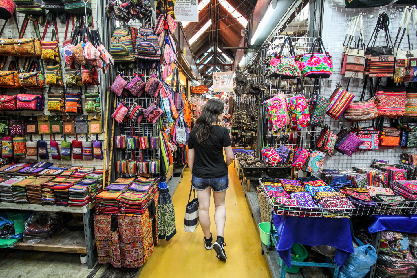 Woman walking through stalls in market covered in bright coloured bags