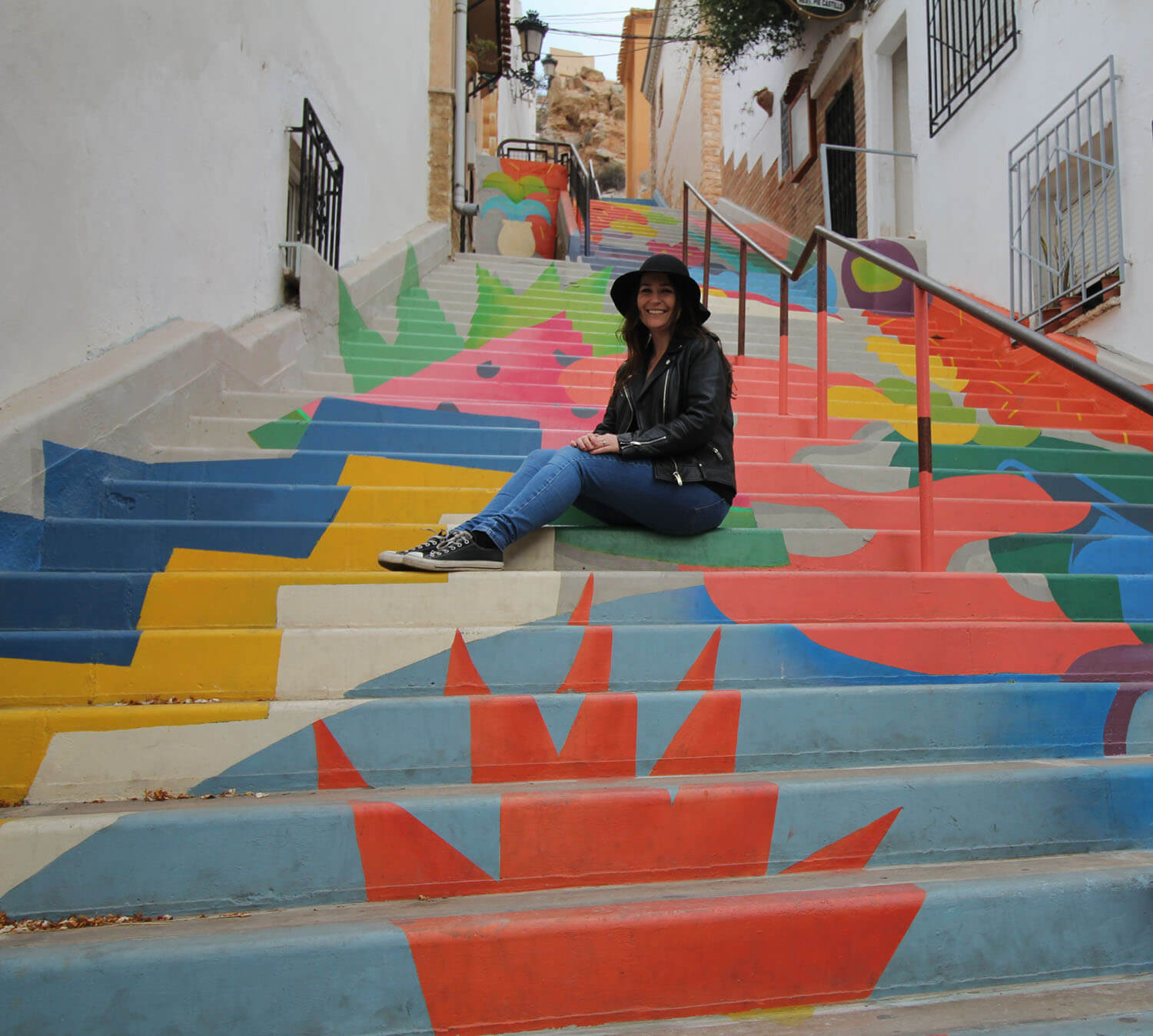 woman sits on steps painted with bright coloured mural