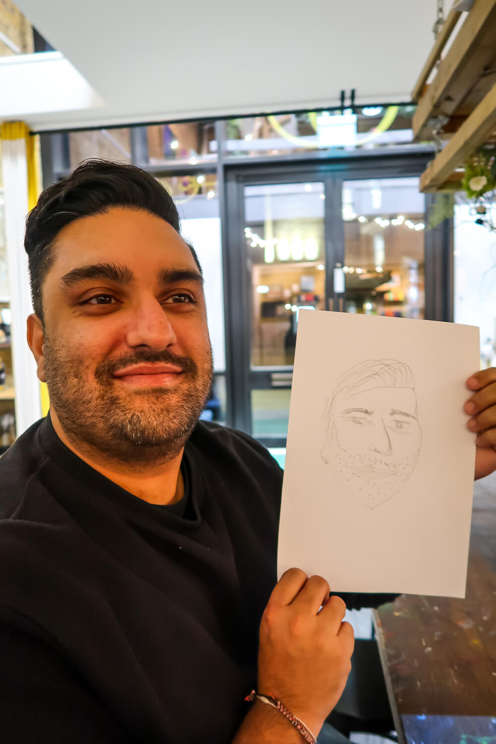 man holds up drawing on paper that vaguely resembles him