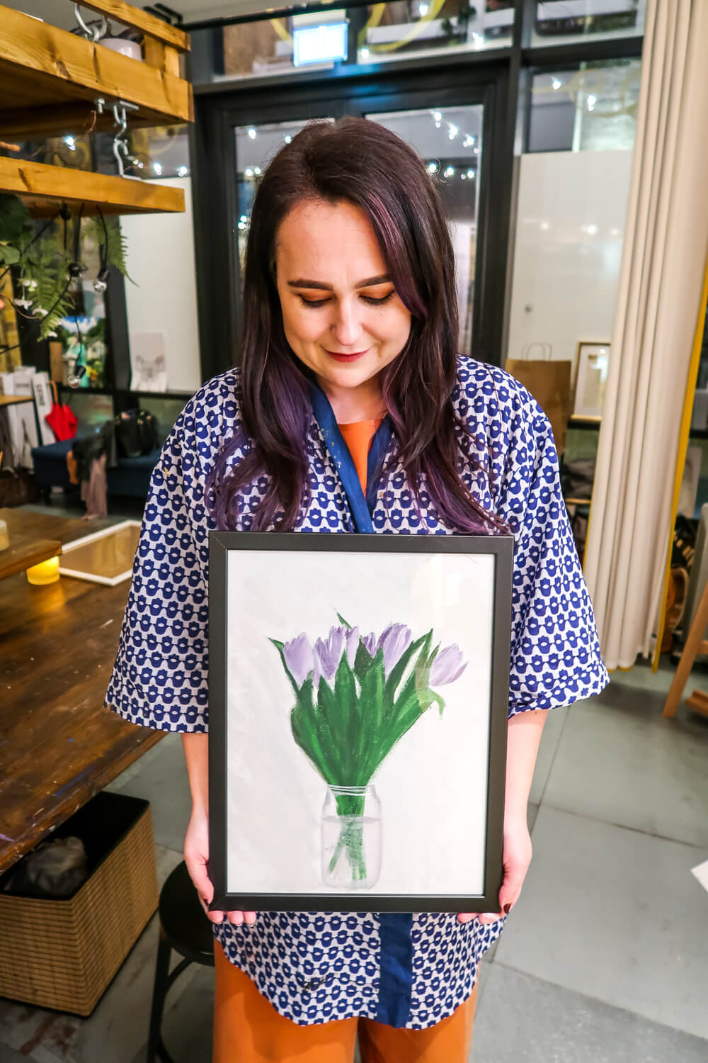 woman holds framed painting of tulips in both hands as she looks down proudly