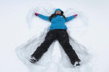 Woman in blue ski jacket lying in the snow making snow angels