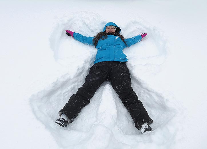 Woman in blue ski jacket lying in the snow making snow angels