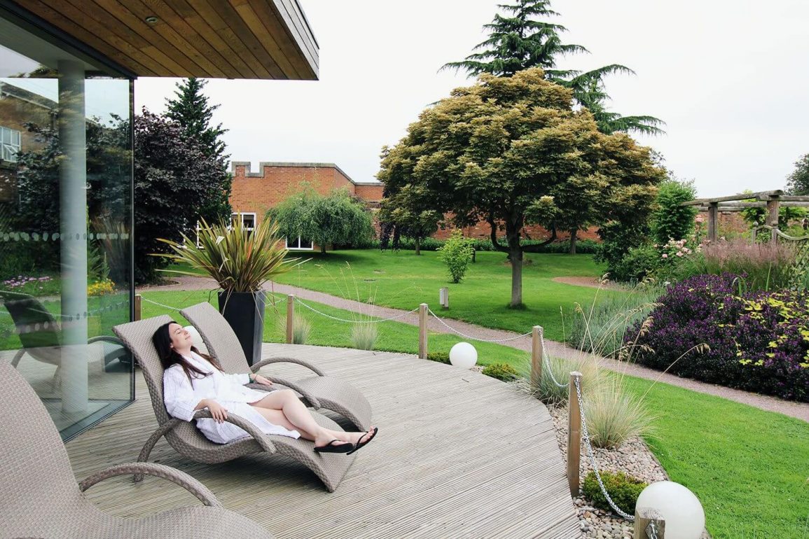 woman in white robe reclines on a lounger in the gardens at a spa
