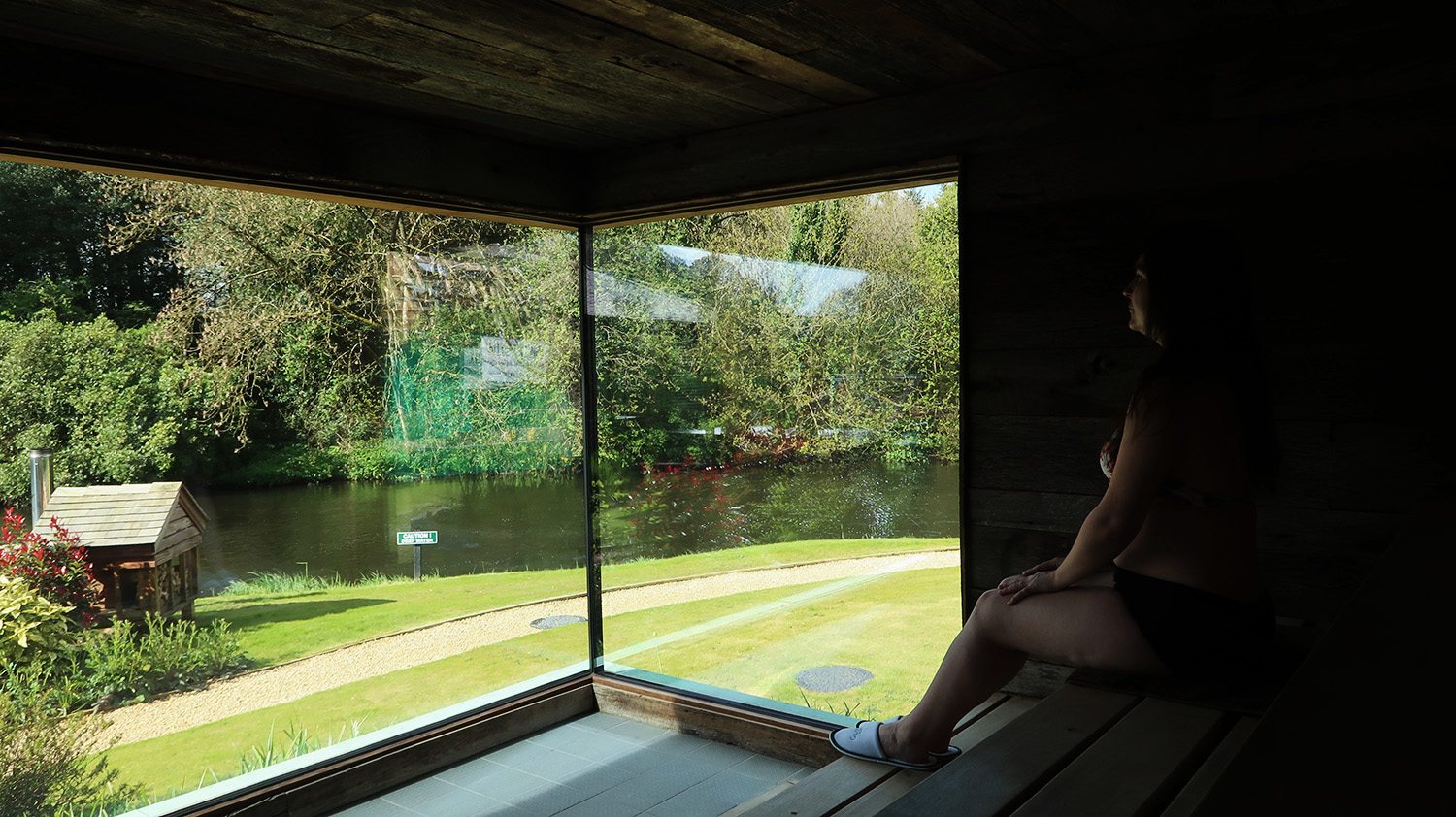 Woman sits in a sauna with dual aspect floor to ceiling windows that look out over a river