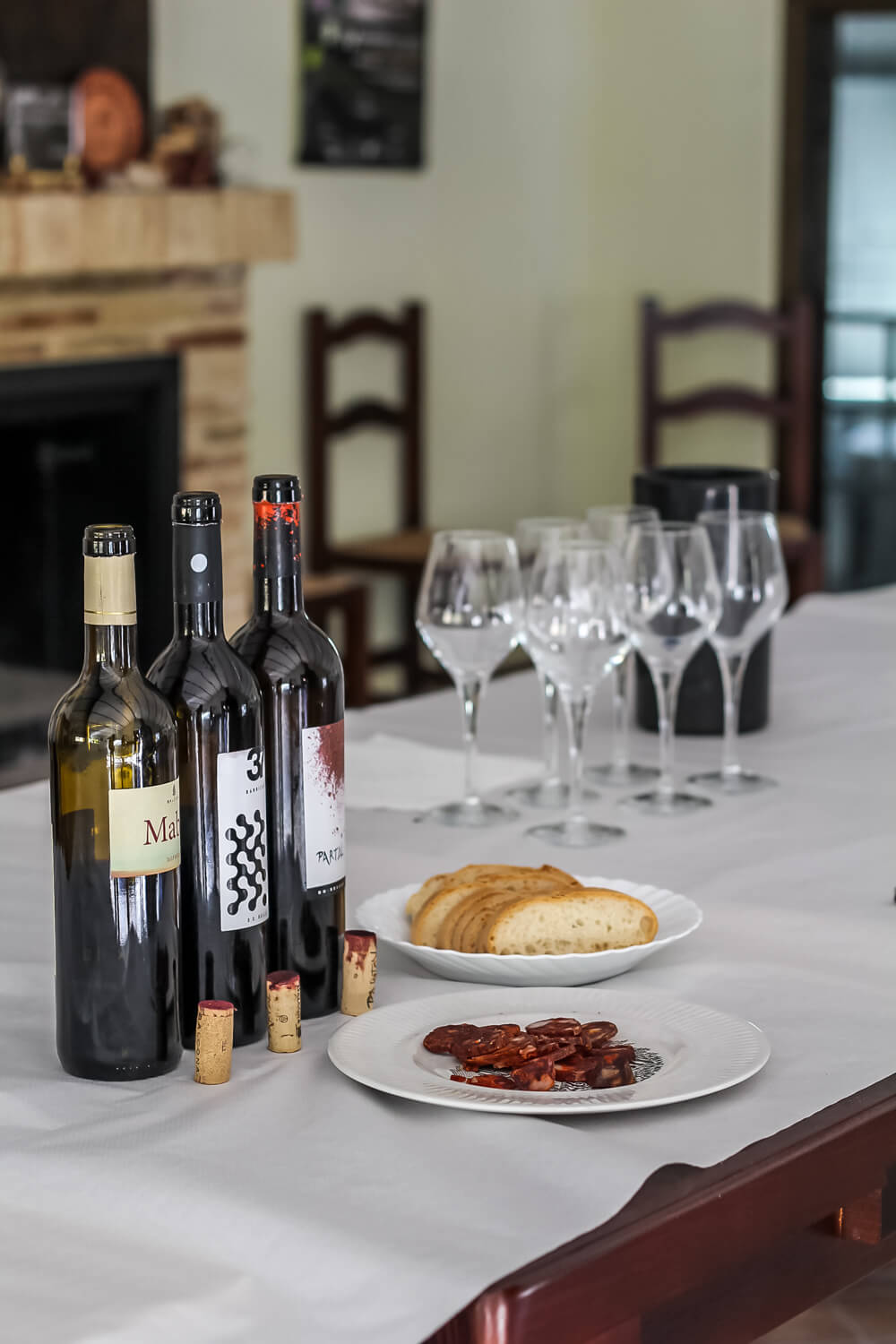table with 3 bottles of wine, bread, chorizo, and glasses