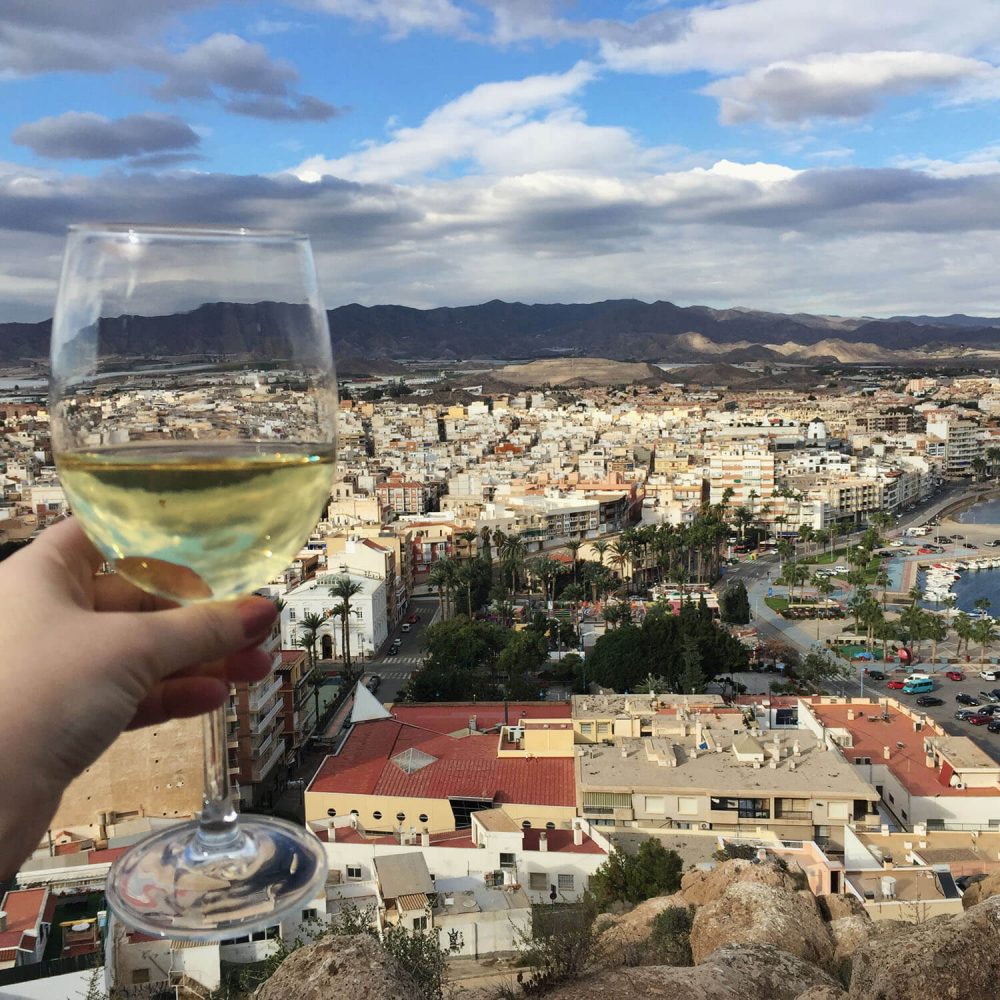 Glass of white wine held up against a backdrop view of the town of Aguilas
