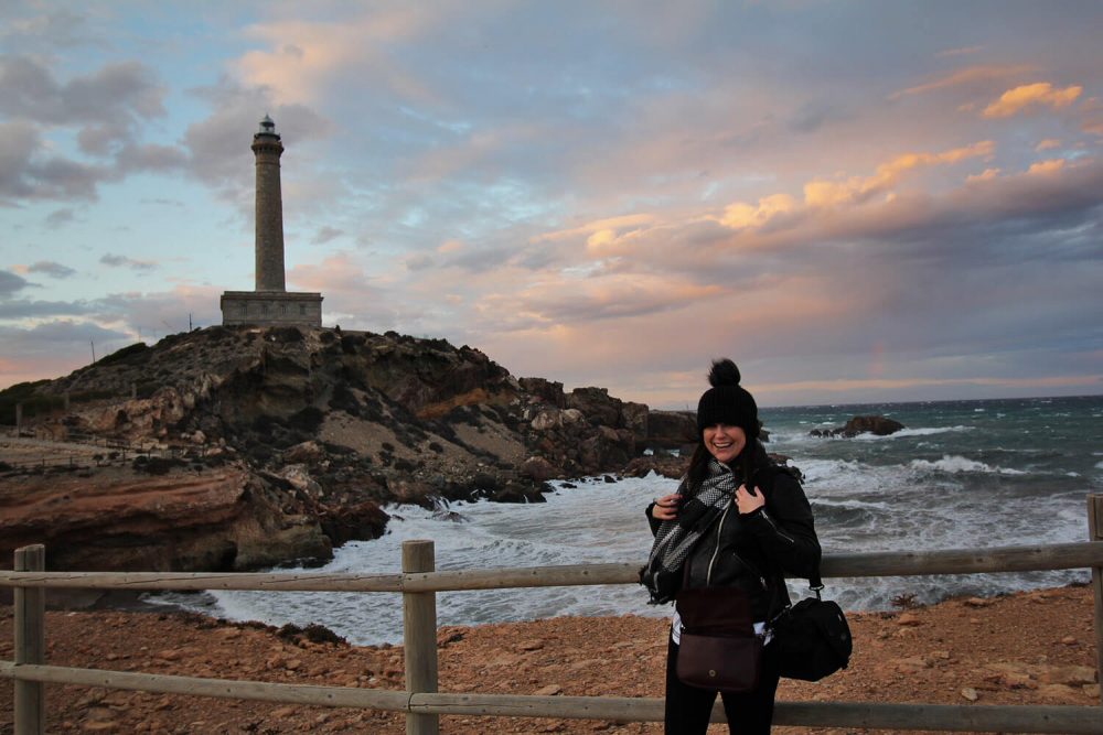 Lighthouse in Murcia as the sun is setting with woman wearing wooly hat smiling in the foreground